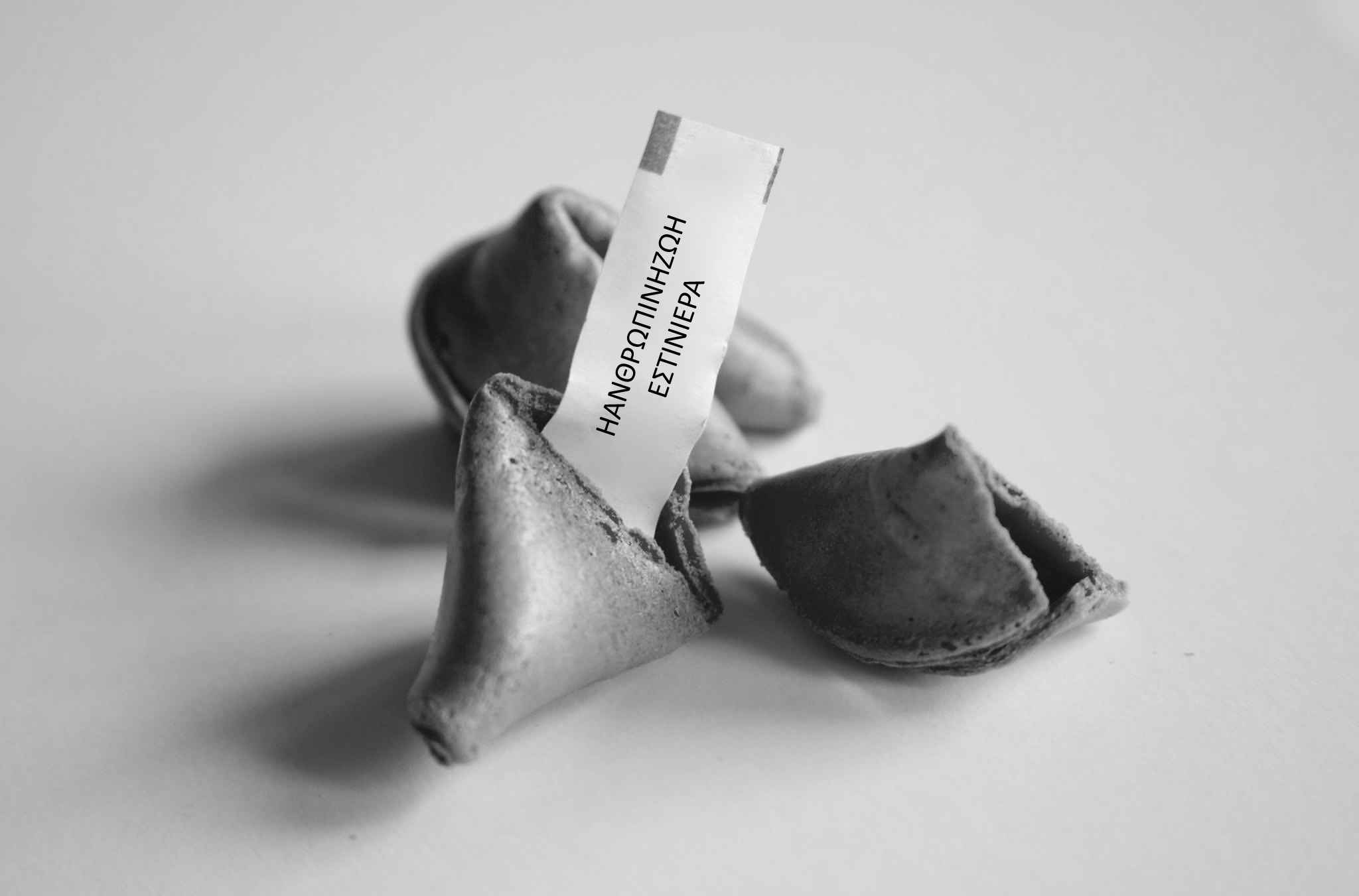 A black and white photograph of a broken fortune cookie. The fortune reads "ΗΑΝΘΡΩΠΙΝΗΖΩΗΕΣΤΙΝΙΕΡΑ".